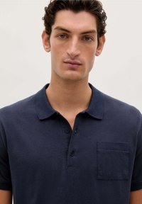 Navyblaues Poloshirt aus Baumwolle, mit klassischem Kragen, dreiknöpfiger Knopfleiste und einer Brusttasche auf der linken Seite. Weiche Textur.
