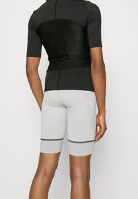 Musta lyhythihainen urheilupaita yhdistettynä vaaleanharmaisiin tiukasti istuviin shortseihin, joissa on mustia vaaka-raitaja ja tekstuuripitoisia yksityiskohtia.