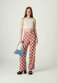 Top court crème, pantalon ample rouge à motifs, sac à main bleu, chaussures à plateforme noires épaisses. Présente un design floral géométrique en blanc cassé.