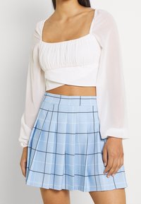 Haut blanc court à manches bouffantes et encolure carrée, associé à une jupe plissée bleu clair avec un motif à carreaux noirs.