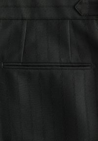 Black suit fabric with vertical pinstripes, featuring a flat pocket and textured weave. Clean lines and tailored design elements evident.