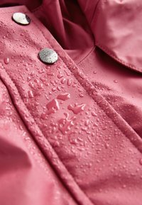 Vízálló rózsaszín dzseki ezüst patentokkal, sima textúrával és gyöngyszerű vízcseppekkel a felületén.