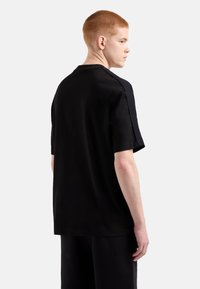 T-shirt nera a maniche corte con dettagli testurizzati sulle spalle, realizzata in tessuto morbido, caratterizzata da una vestibilità rilassata e un design minimalista.