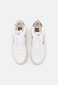Zapatillas blancas con acentos en rosa y púrpura, textura perforada, cordones planos y suela de goma beige. Presenta una etiqueta con el logo en el interior.