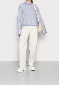 Pullover azzurro chiaro in maglia con motivo a zigzag, abbinato a pantaloni beige a gamba larga e sneakers bianche spesse. Borsa chiara appoggiata sulla spalla.