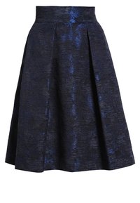 En plisserad kjol i mörkblått tyg med ett texturerat mönster. Midjan är åtsittande, vilket gör att kjolen svänger något vid fållen.