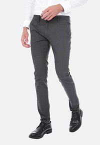 Pantaloni grigi a fantasia con vestibilità slim e texture liscia, abbinati a scarpe in pelle nera. I pantaloni presentano tasche e passanti per cintura.