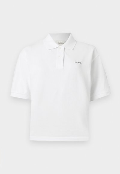 Λευκό πόλο με κοντά μανίκια, γιακά, δύο κουμπιά και μικρό κέντημα με το κείμενο «CLOSED» στο αριστερό στήθος και μέσα στον γιακά.