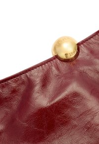 Bolso de mano de cuero rojo con acabado texturizado, que presenta un cierre redondeado dorado con "Furla" grabado en él. Bordes suaves, diseño minimalista.
