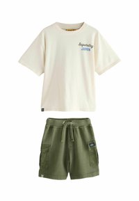 Baltas kokvilnas t-krekls ar īsām piedurknēm un zilu tekstu "Superdry Japan", saskaņots ar zaļiem kokvilnas šortiem, kuriem ir sānu kabatas un aukla.