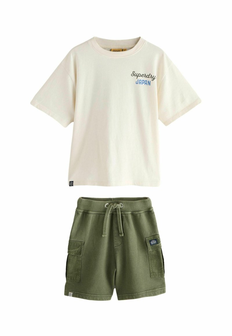Baltas kokvilnas t-krekls ar īsām piedurknēm un zilu tekstu "Superdry Japan", saskaņots ar zaļiem kokvilnas šortiem, kuriem ir sānu kabatas un aukla.