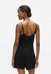 Sort tanktop lavet af blødt stof, med tynde stropper, en afslappet pasform og en rund bund. Samlet med matchende sorte shorts.