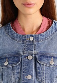 Spijkerjasje met een klassieke snit, blauwe stof, twee borstzakken, zilverkleurige knopen en een getextureerde roze binnenlaag.