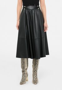 Gonna midi nera in pelle A-line con vita arricciata e bottoni decorativi, abbinata a stivali alti fino al ginocchio in pelle di serpente metallica.