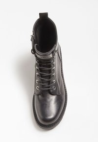 Bottine en cuir noir avec un laçage à l'avant, œillets en métal et une sangle décorative près du haut. Elle présente une texture lisse et un bout rond.