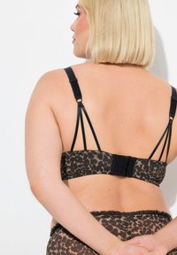 Bra dengan motif leopard yang memiliki tali hitam tipis, pengait yang dapat disesuaikan, dan bahan yang tekstur. Desainnya menampilkan punggung rendah dan jahitan yang halus.