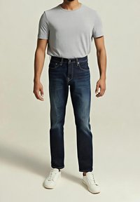 Šedé tričko s krátkým rukávem, tmavě modré džíny s rovným střihem a bílé tenisky. Klasický střih, měkká textura, bez viditelných vzorů či ozdob.