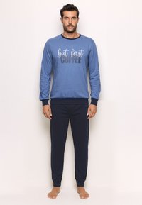 Blue long-sleeve sweatshirt with "but first coffee" text, paired with dark navy pants. Both items feature a soft, smooth texture.