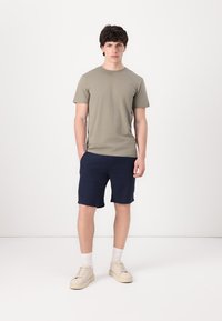 Ελαιόχρωμο βαμβακερό t-shirt, ναυτικές σορτσάκια, κρεμ αθλητικά παπούτσια με άσπρες κάλτσες. Χαλαρή εφαρμογή, κοντά μανίκια, μίνιμαλ σχέδιο, μαλακή υφή.