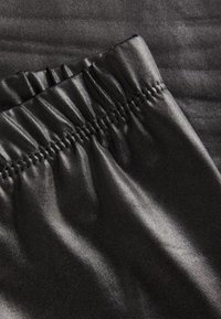 Tejido negro con una cintura elástica fruncida, textura suave y un brillo sutil. El material parece ligero y flexible.