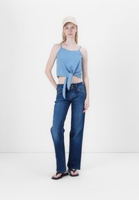 Top in denim azzurro chiaro, accorciato, con dettaglio di nodo frontale, abbinato a jeans a vita alta in denim blu scuro a gamba larga e ciabatte nere.