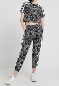 Svart- och vittmönstrad croppad t-shirt och matchande joggers med sidostriper, med geometriska mönster och elastiska manschetter, i kombination med vita sneakers.