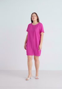 Vestido rosa de mangas curtas com um decote redondo simples, corte descontraído e textura suave. Usado com sandálias de salto brancas.