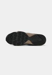 Black and tan athletic shoe sole featuring a textured rubber pattern, grooves for traction, and a visible logo on the lateral side.