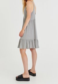 Vestido gris sin mangas con un dobladillo acampanado, hecho de tela suave. Combinado con zapatos de plataforma negros tipo deslizantes, que presentan un diseño sencillo.
