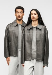 Γκρι δερμάτινα μπουφάν με άνετη γραμμή, που διαθέτουν μυτερό γιακά, κεντρικό φερμουάρ και πλαϊνές τσέπες, φορεμένα πάνω από γκρι πουκάμισα και φόρμες.