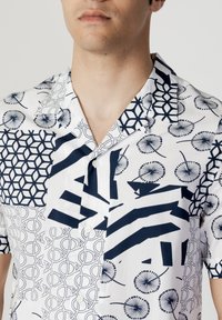 Korte mouw shirt met een mix van marineblauwe geometrische en bloemachtige patronen op een witte katoenen stof, met een inspringende kraag en knopen.