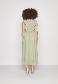 Vestido midi verde claro con hombros volantes, tejido texturizado y cintura ceñida. Combinado con sandalias metalizadas de tacón.