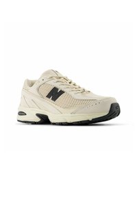 Beiga sportskor i mesh och mocka, med en svart 'N' logotyp, vadderad krage och texturerad gummisula.