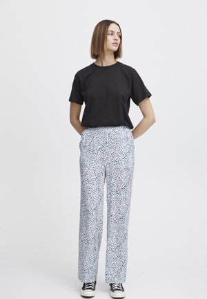Black short-sleeve t-shirt paired with loose-fitting, patterned trousers in blue and white, featuring a spotted design. Black and white sneakers.