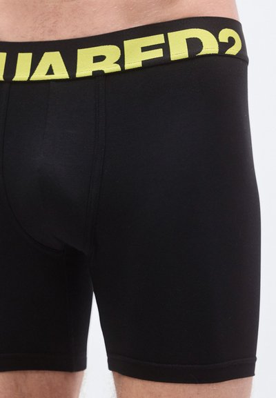 Boxers negros con pretina con logotipo amarillo, fabricados con tela elástica, de diseño ajustado y textura suave.