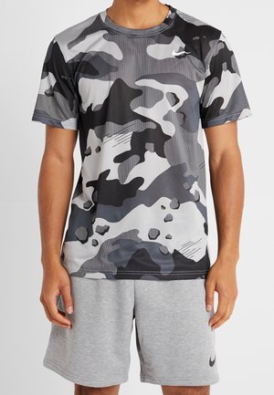 Homme portant un t-shirt à manches courtes imprimé camouflage noir, blanc et gris et un short gris uni avec un petit logo Nike.