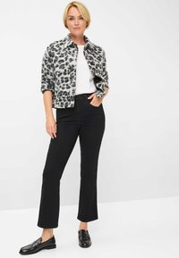 Jasje met luipaardprint in grijs en zwart, witte t-shirt, zwarte rechte jeans en zwarte instappers. Zachte textuur, casual pasvorm.