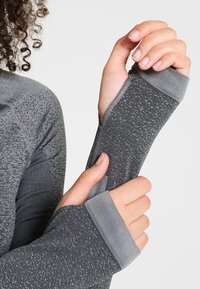 Szary sportowy top z długim rękawem, wykonany z teksturowanej tkaniny, z otworami na kciuki przy mankietach oraz kontrastowymi akcentami w prążki na rękawach.