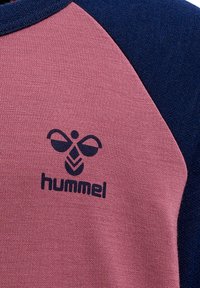 Lyserød og marineblå sweatshirts med en tekstureret stof. Har raglanærmer og et fremtrædende sort logo med et stiliseret bierdesign.