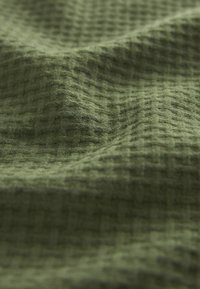 Gestructureerde groene stof met een ruitpatroon, die een zachte, geweven uitstraling en subtiele variaties in kleur en textuur toont.