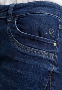 Jeans de mezclilla en azul oscuro con un sutil bordado de corazón en el bolsillo delantero, que presentan bolsillos estándar y un corte clásico.