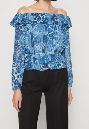 Femme portant un chemisier bleu épaules dénudées avec des volants et un imprimé mixte paisley et léopard, associé à un pantalon noir.