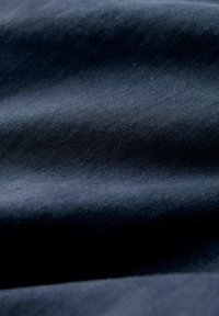 Nahaufnahme eines dunkelblauen Denim-Stoffes, der eine feine diagonale Webstruktur und subtile Falten im Material zeigt.