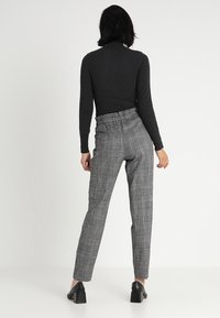 Černý žebrovaný rolák spárovaný s šedými kostkovanými kalhotami s vysokým pasem. Kalhoty mají elastický pás a rovný střih. Černé boty na blokovém podpatku.