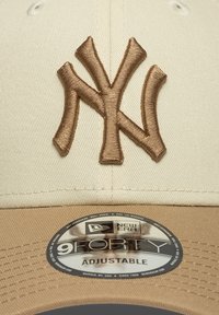 Μπεζ καπέλο μπέιζμπολ με ανάγλυφο, μπρούντζινο κεντημένο λογότυπο NY, που διαθέτει στρογγυλεμένο στέμμα και ρυθμιζόμενο λουράκι. Υφή στη γείσο με ετικέτα.