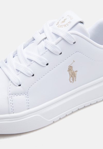 Hvit lær-sneaker med hvite lisser og gullbrodert Polo Ralph Lauren-logo på siden og tungen.