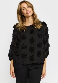 Sort gennemsigtig bluse prydet med 3D rosenapplikationer, med rund halsudskæring og 3/4 ærmer. Blødt, tekstureret stof.