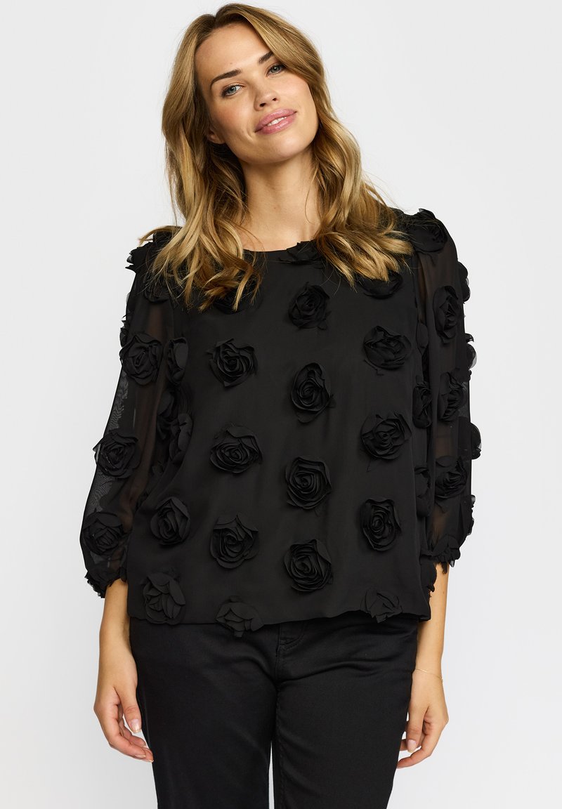Sort gennemsigtig bluse prydet med 3D rosenapplikationer, med rund halsudskæring og 3/4 ærmer. Blødt, tekstureret stof.