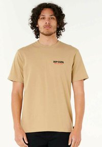Tan kortemouw T-shirt van zachte stof. Heeft een klein zwart "RIPCURL" logo op de linkerborst. Eenvoudig ontwerp, reguliere pasvorm.