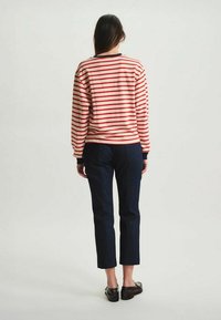 Haut à manches longues rayé rouge et crème avec des poignets côtelés, associé à un jean droit bleu foncé et des chaussures noires à enfiler.